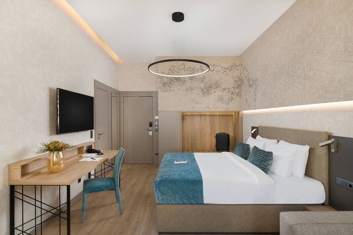 A modern hotel room with a bed, desk, chair, and a flat-screen TV.