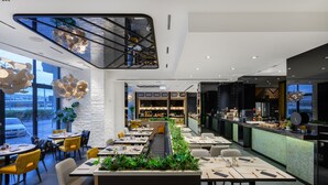 A modern restaurant with a long counter, seating area, and a view of the street. - Hotel Vision (Budapest)