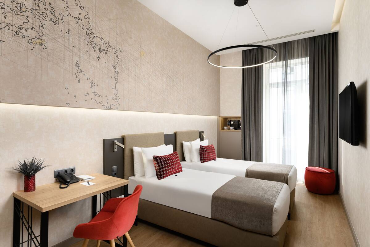 A modern hotel room with two beds, a desk, a chair, a map on the wall, and a TV.