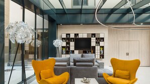 A modern living room with a sofa set, two yellow armchairs, a coffee table, and a TV against a wooden wall. - Hotel Vision (Budapest)
