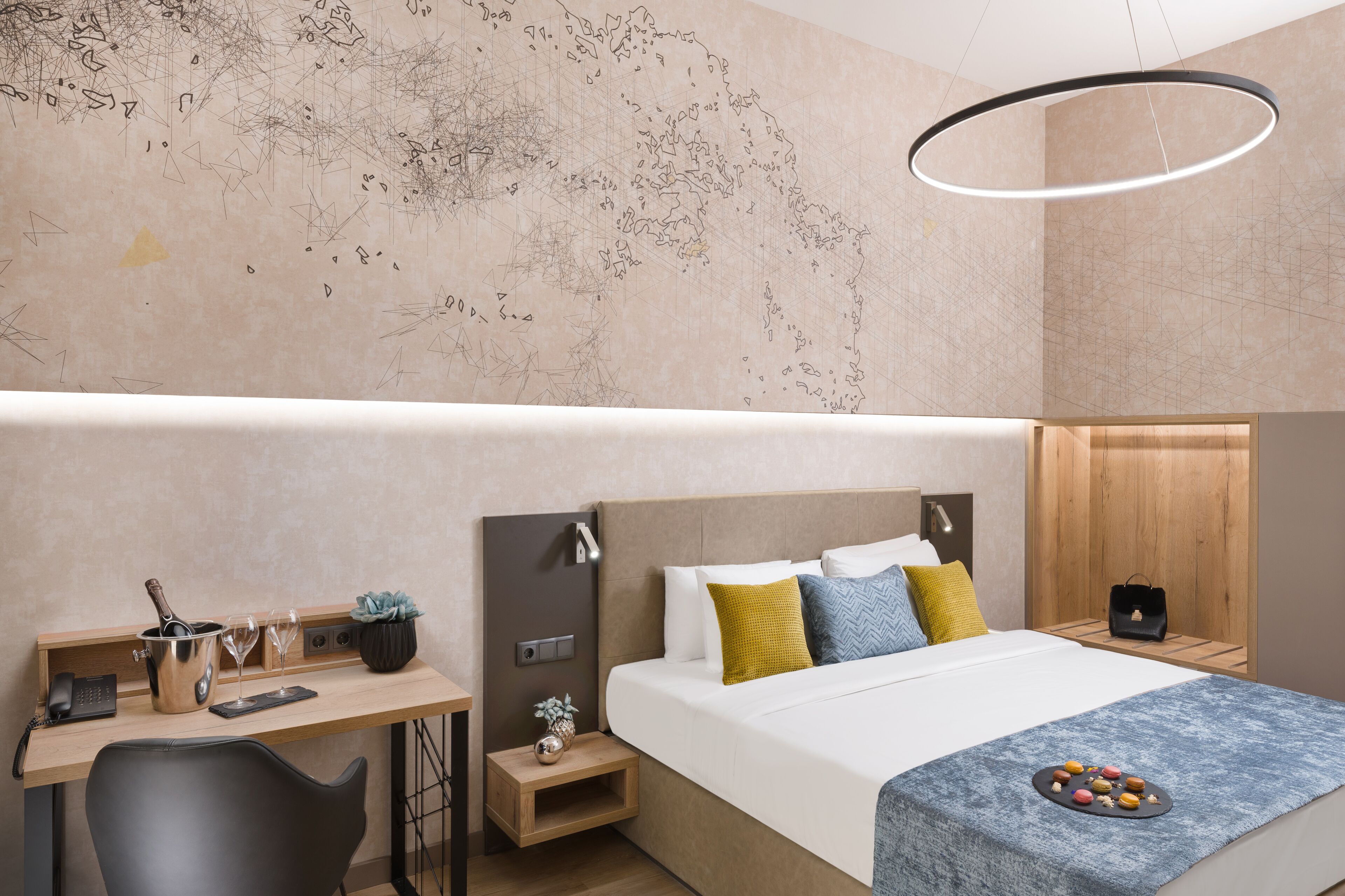 Habitación de hotel moderna con una cama grande, un escritorio con teléfono y una botella de champán, una mesita con un jarrón, y un mapa en la pared.