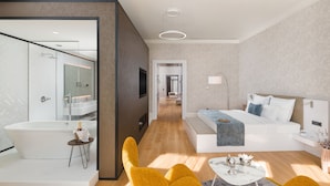 A modern hotel room with a large bed, a sitting area with a coffee table, a bathtub, and a separate bathroom with a glass shower enclosure. - Hotel Vision (Budapest)