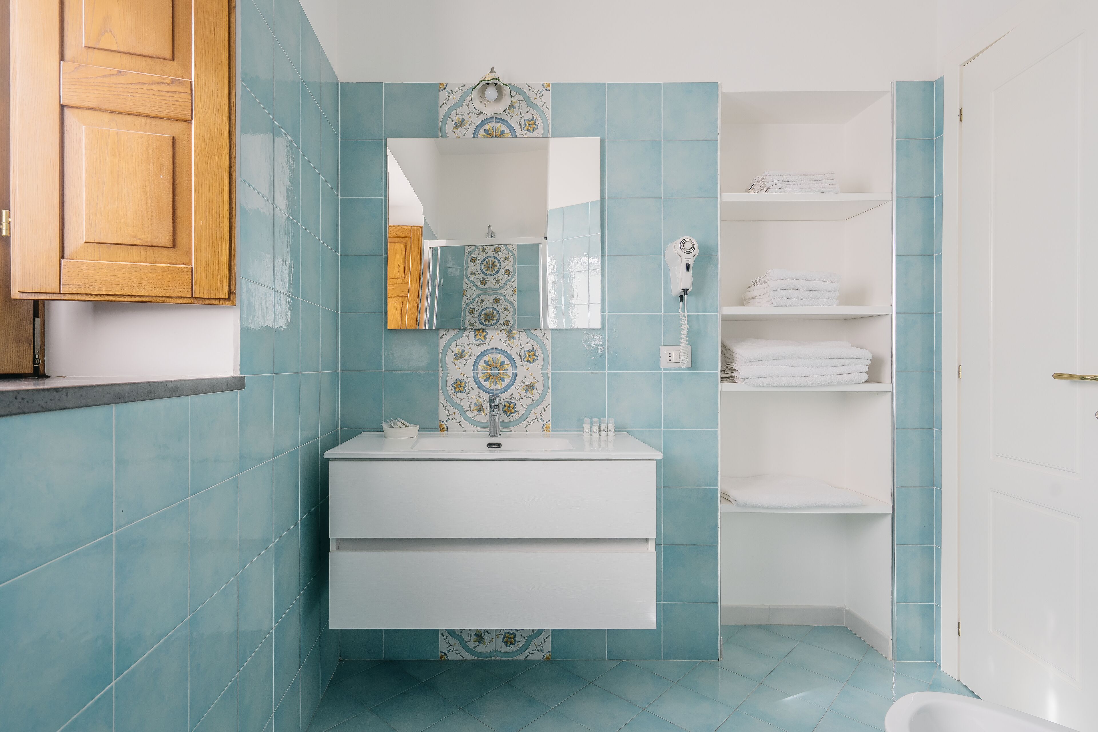 Un baño con lavamanos blanco, espejo, toallero y zona de ducha.
