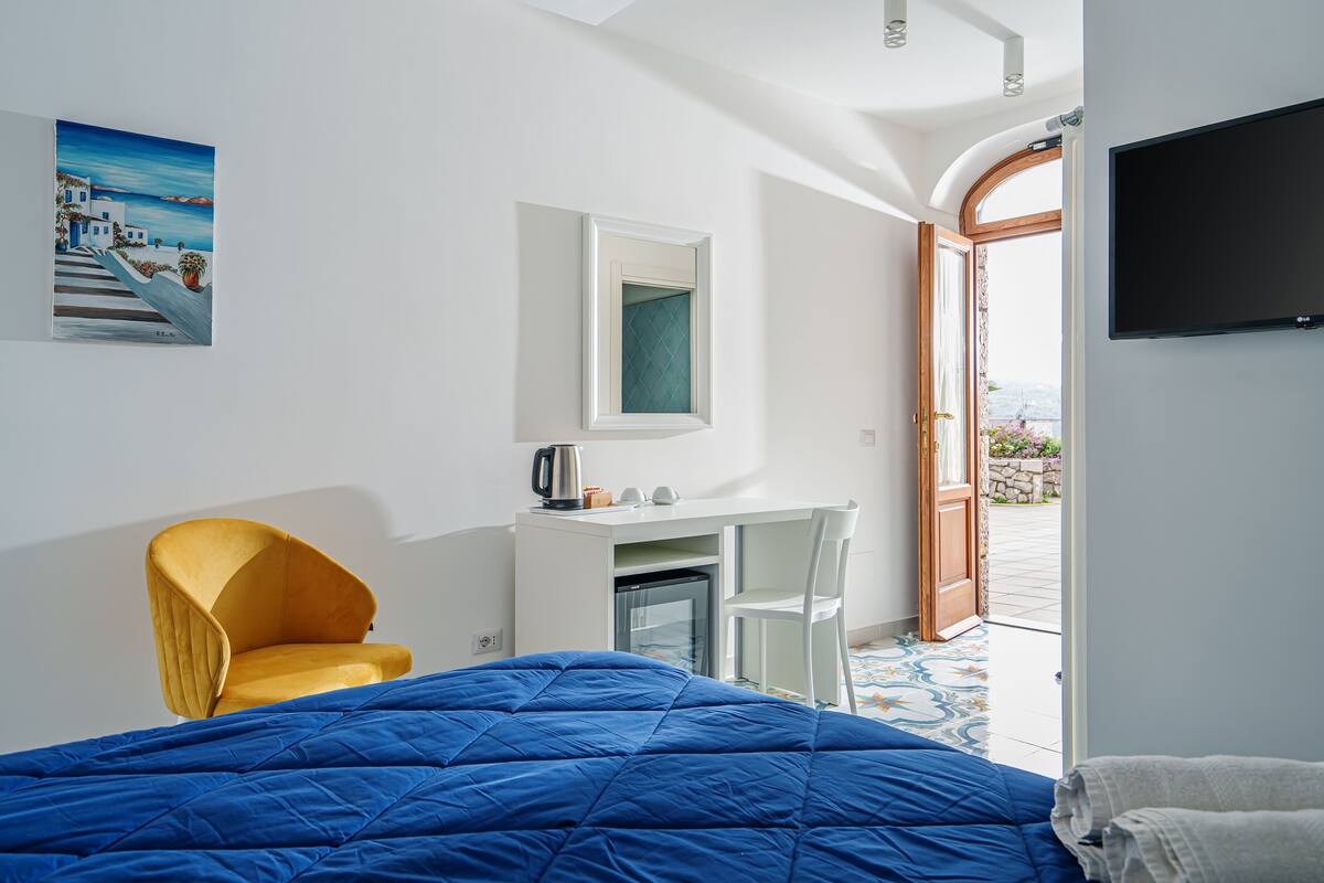 A bedroom with a blue bed, a yellow chair, a desk, and a TV.