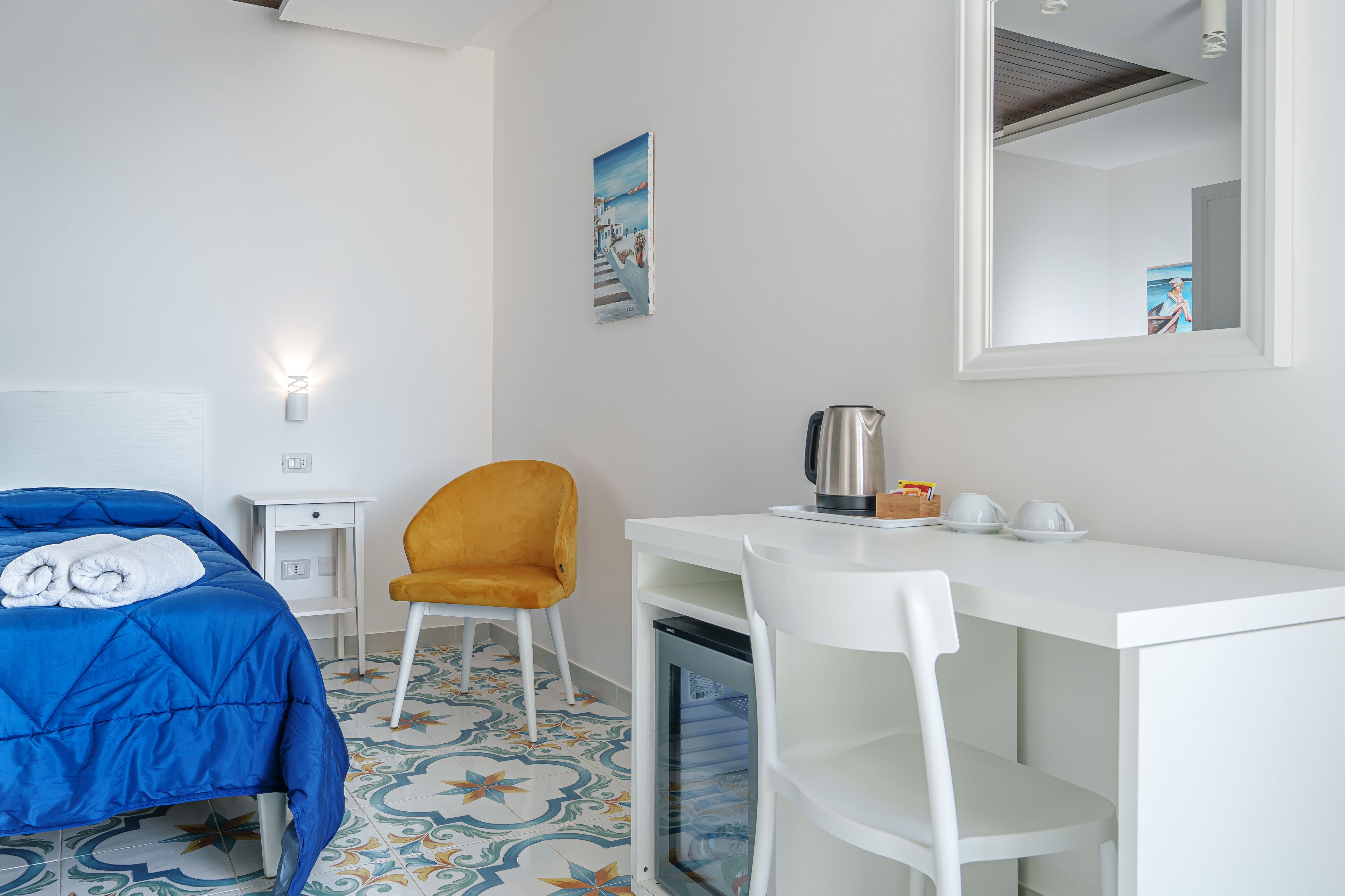 A hotel room with a bed, a desk, a chair, a coffee maker, and a mirror.