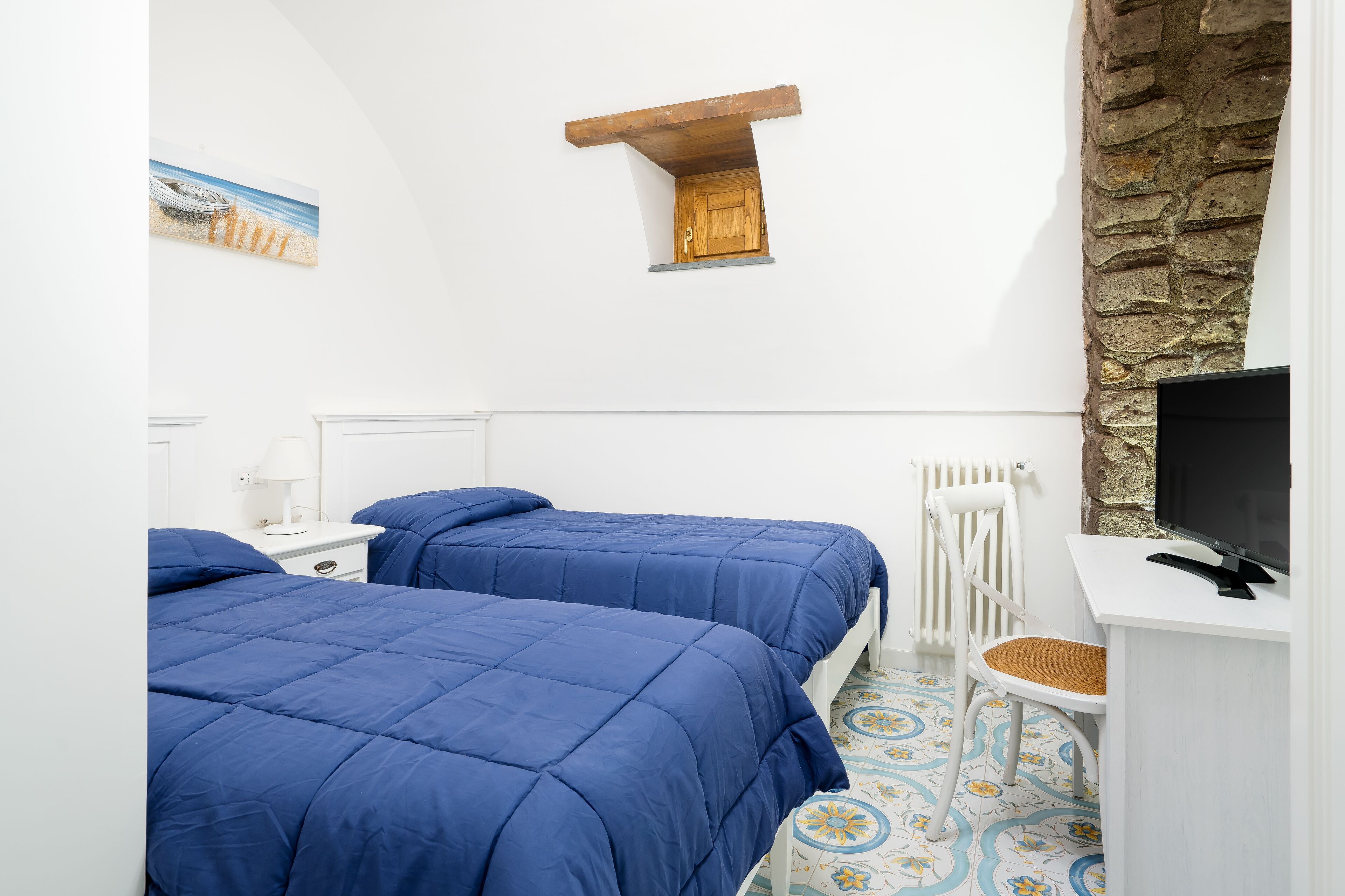 Een slaapkamer met twee bedden, een bureau, een televisie en een stenen muur.