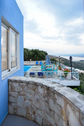 A stone-walled balcony with a pool, blue chairs, and a view of the sea. - Marika Studios & Apartments (Apokoronas)