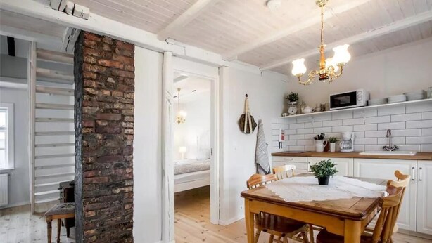 Une cuisine moderne avec des meubles blancs, un mur d’accent en briques et un coin repas comprenant une table et des chaises en bois.