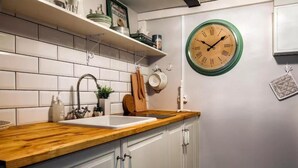 Une cuisine avec des meubles blancs, un plan de travail en bois, un évier et une horloge fixée au mur.