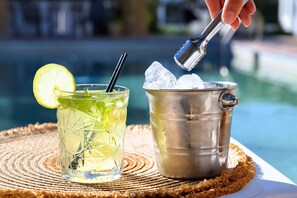 Un vaso con una rodaja de limón y una pajita, junto a un balde de metal con cubitos de hielo.