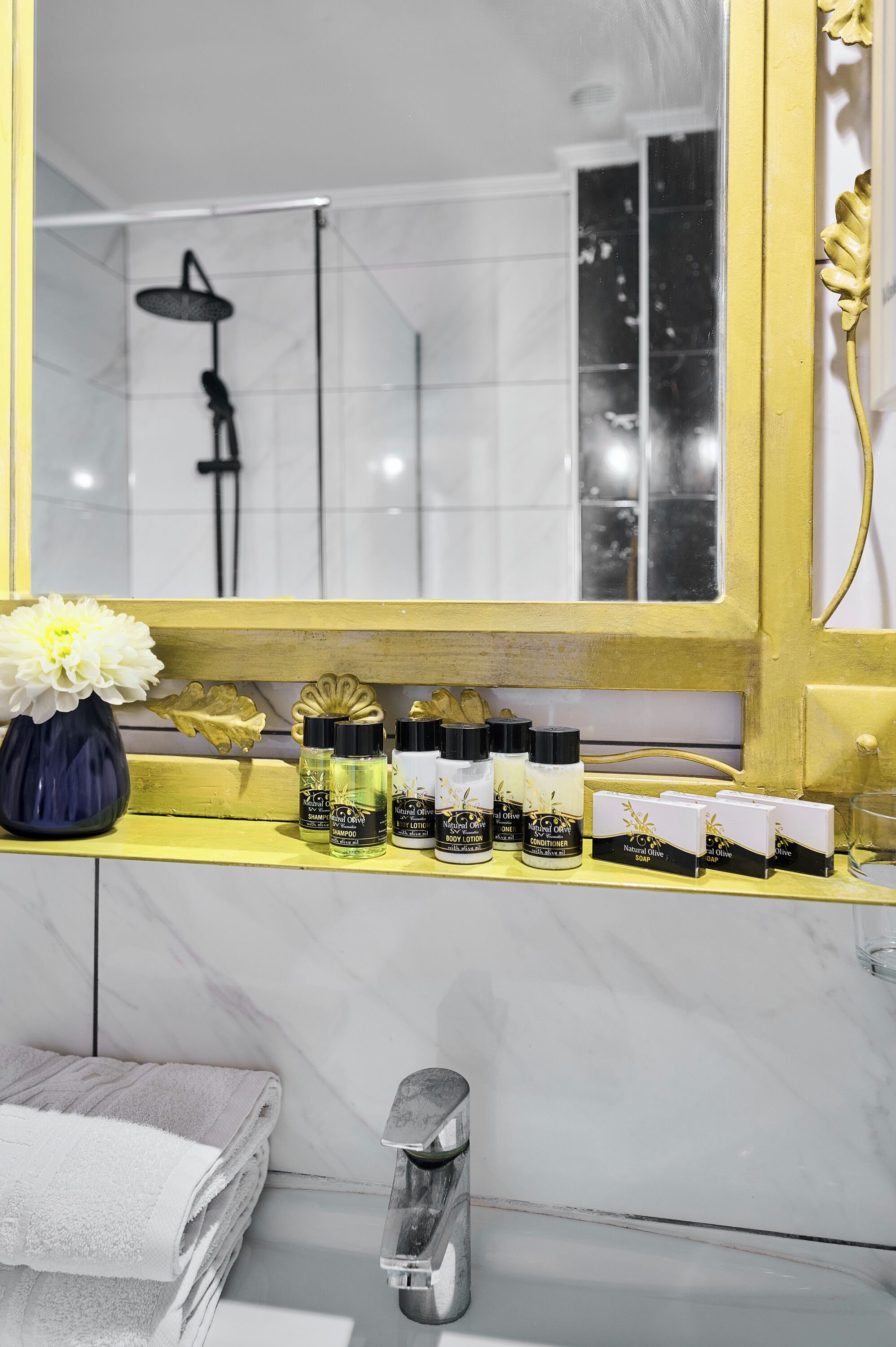 A bathroom vanity with a mirror, a vase of flowers, and a row of toiletries.