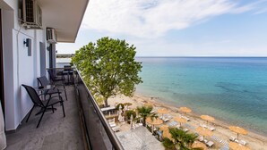 Een balkon met buitenmeubilair, met uitzicht op een strand met parasols en ligbedden.