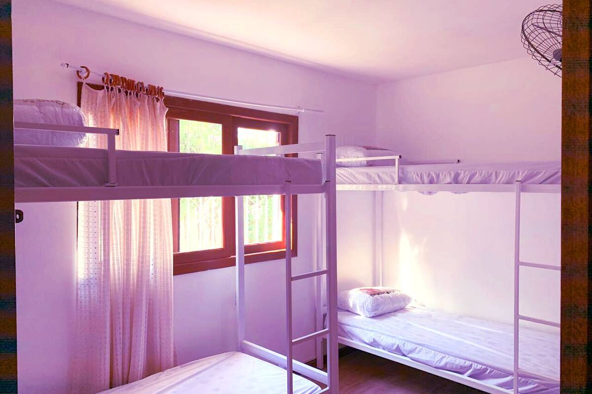 Une chambre avec un lit superposé, une fenêtre, des rideaux et un ventilateur.