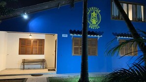 A hostel with a blue exterior, a bench outside, and a palm tree in the foreground. - Lampião Hostel (Florianópolis)