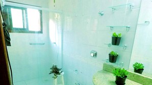 A bathroom with a toilet, sink, and shower. There are potted plants on the countertop and shelves. - Lampião Hostel (Florianópolis)