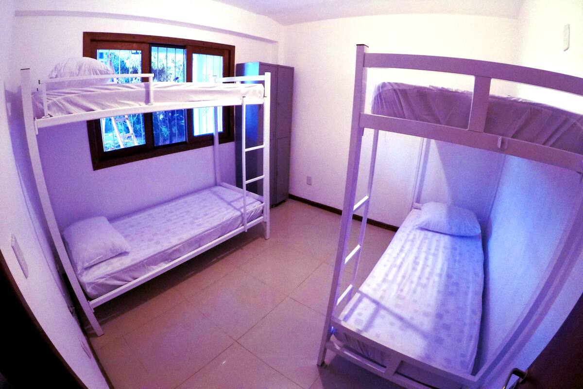 Une chambre avec deux lits superposés, une fenêtre avec des stores et un petit placard.