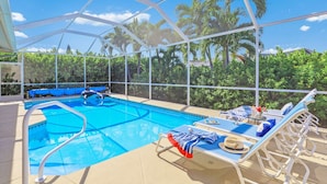 Une piscine intérieure à l’eau d’un bleu cristallin, entourée d’une structure de toit blanche et de palmiers visibles à travers les parois transparentes.