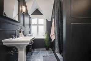 Ein modernes Badezimmer mit einem weißen Waschbecken, dunklen Wänden, einem großen Spiegel und einem Fenster.