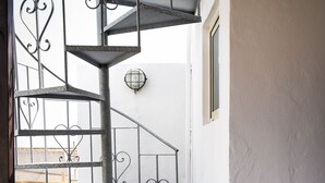 Eine Wendeltreppe mit aufwendiger Metallreling in einem schmalen Gang mit weißen Wänden und Fliesenboden.