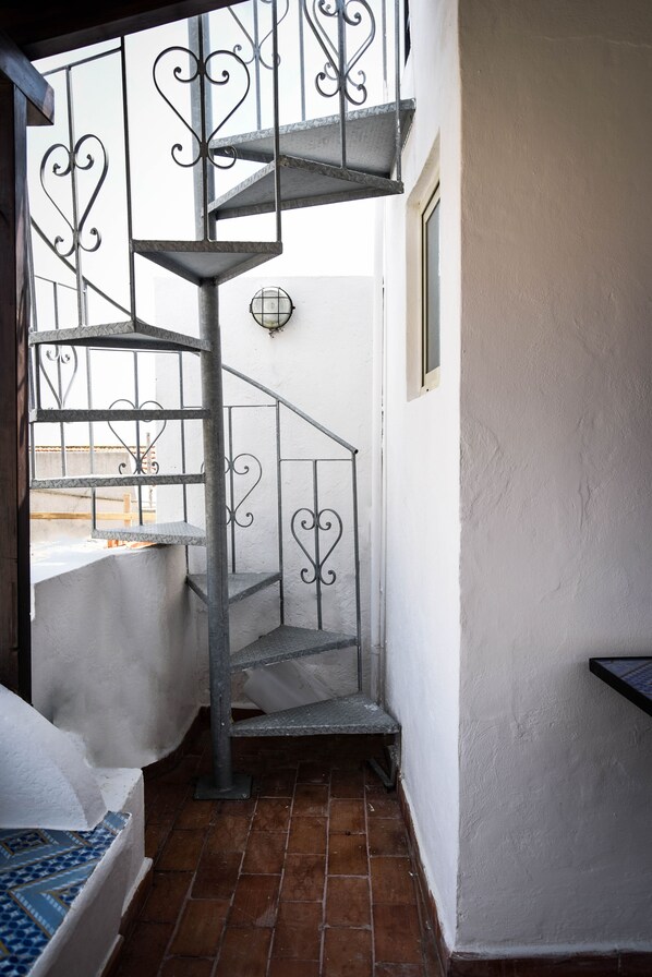 A spiral staircase with ornate metal railings in a narrow hallway with white walls and a tiled floor. - House in Lipari center with sea view (Lipari)