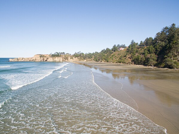 Une plage à l’eau claire, avec un rivage sablonneux et une colline boisée en arrière-plan.