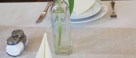 Une table à manger ornée d’un vase en verre transparent contenant une seule rose, de deux salerons et poivriers, et d’une serviette pliée.