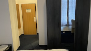Una habitación de hotel con una cama, una puerta de madera y vistas a través de una ventana con cortinas.