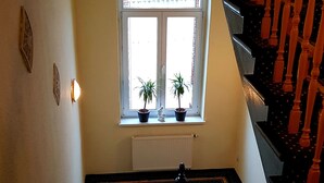Una escalera con alfombra estampada, barandillas de madera y un ventanal con dos macetas.