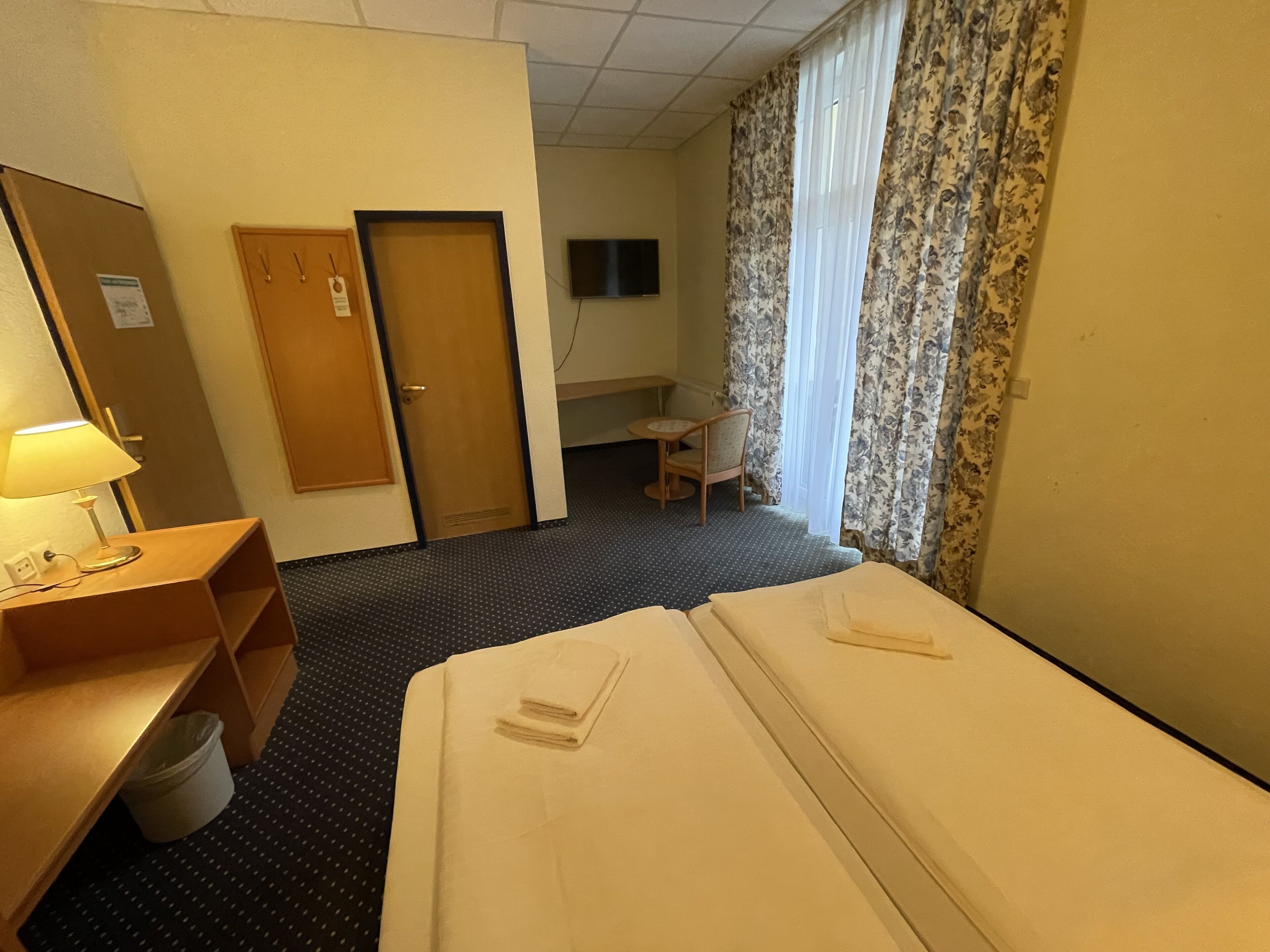 Una camera d'albergo con un letto, una scrivania, una sedia, una televisione e una porta.