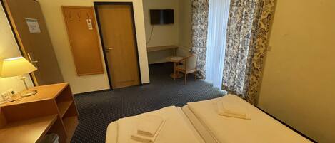 Una camera d'albergo con un letto, una scrivania, una sedia, una televisione e una porta.