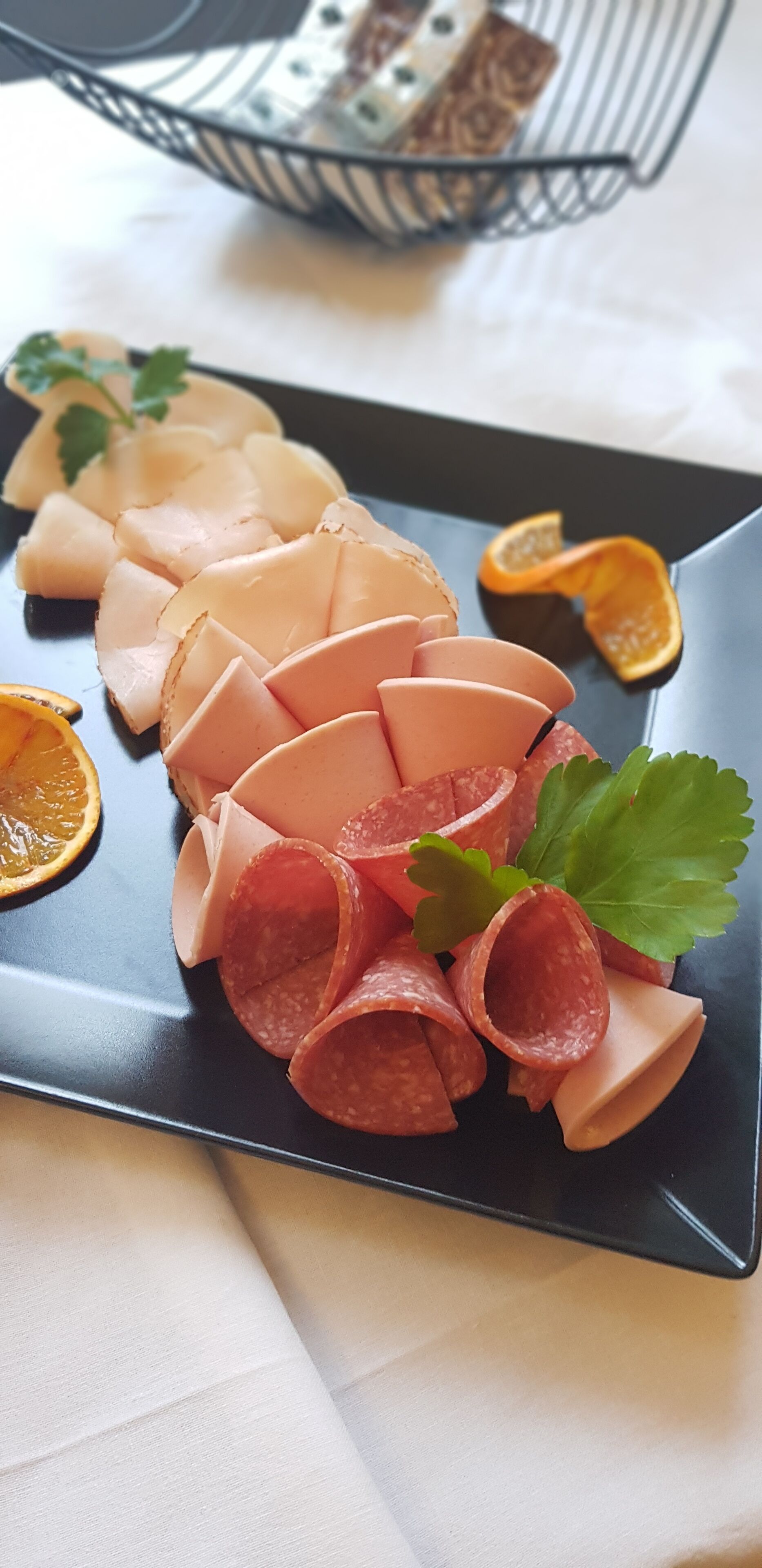 Un plato negro con carnes en rodajas y una guarnición de perejil.