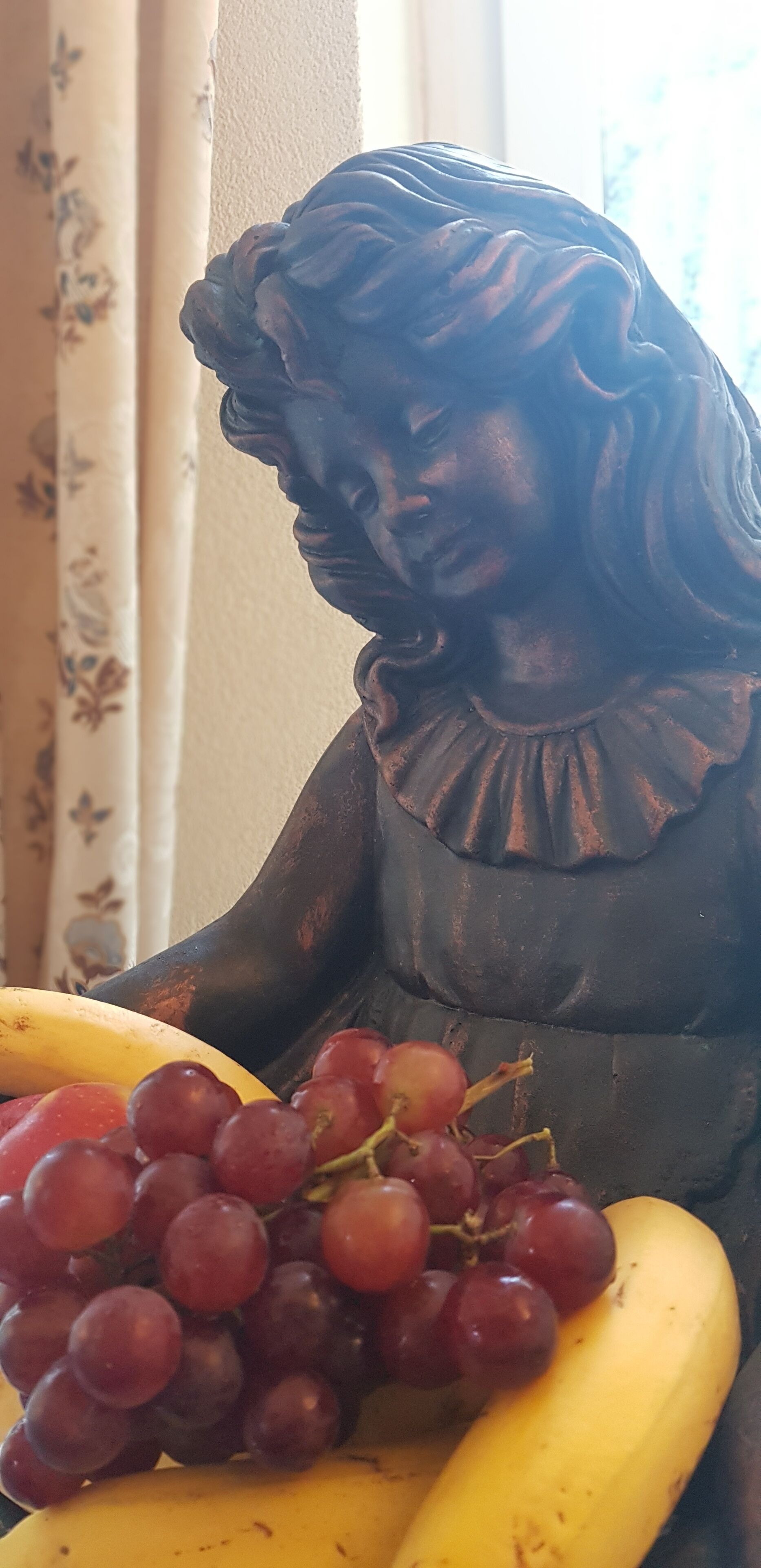 A statue of a woman holding a bunch of grapes and a banana.