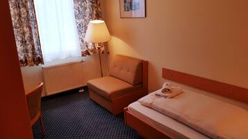 Et hotelværelse med seng, stol, skrivebord, lampe og radiator.