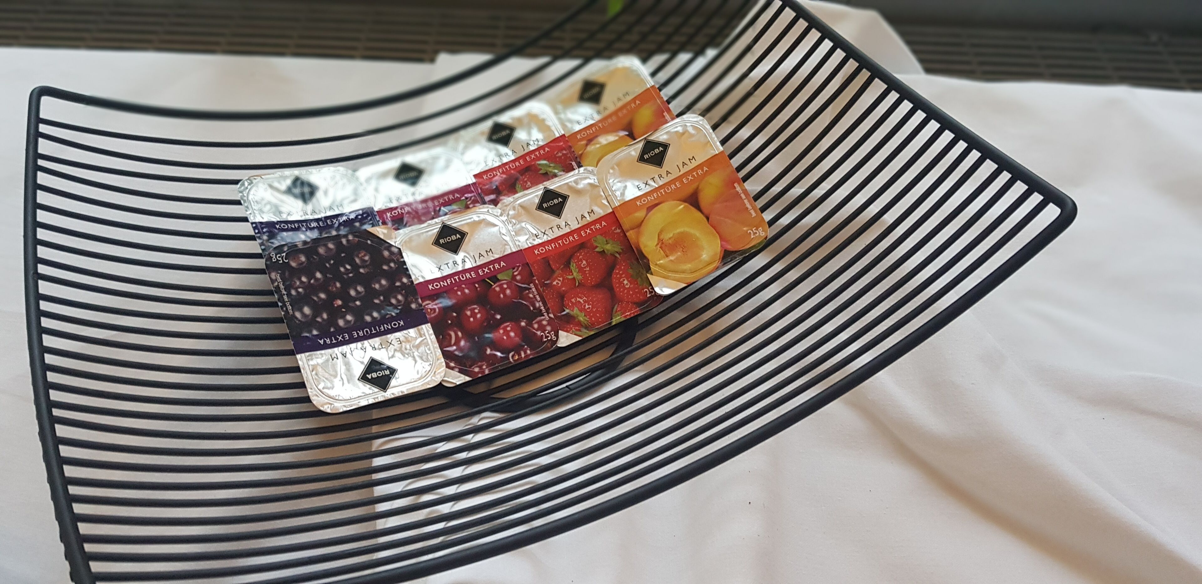 Un panier en fil de fer noir contenant divers pots de confitures et de pâtes à tartiner.