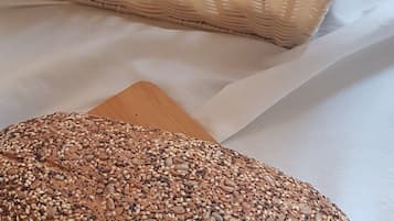 Una cesta de mimbre llena de panes variados y una hogaza de pan con semillas sobre una tabla de madera.