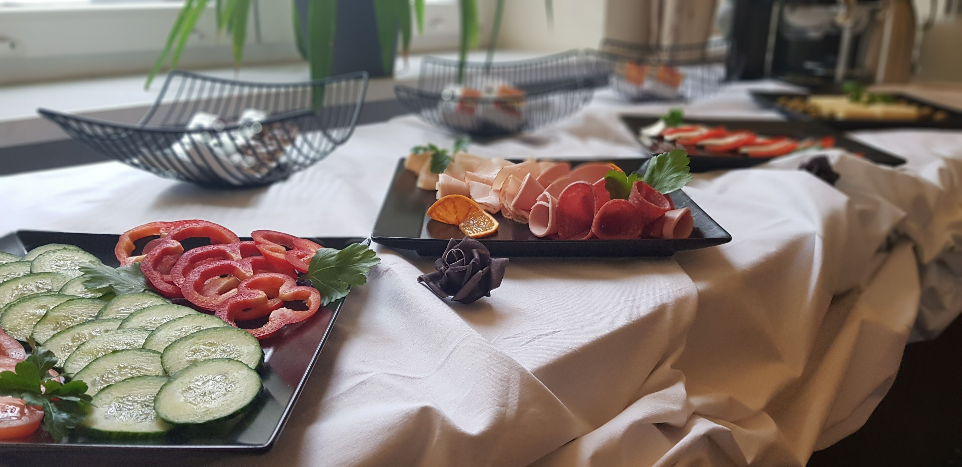 A buffet table with various food items including sliced cucumbers, tomatoes, and meat.