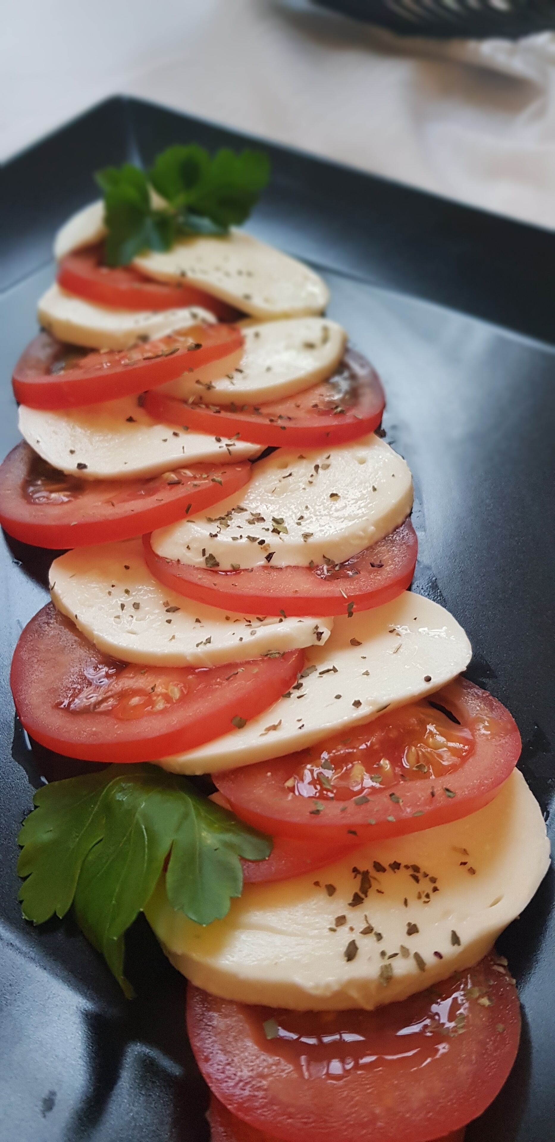 Une assiette noire sur laquelle sont joliment disposées des tranches de tomates et du fromage.
