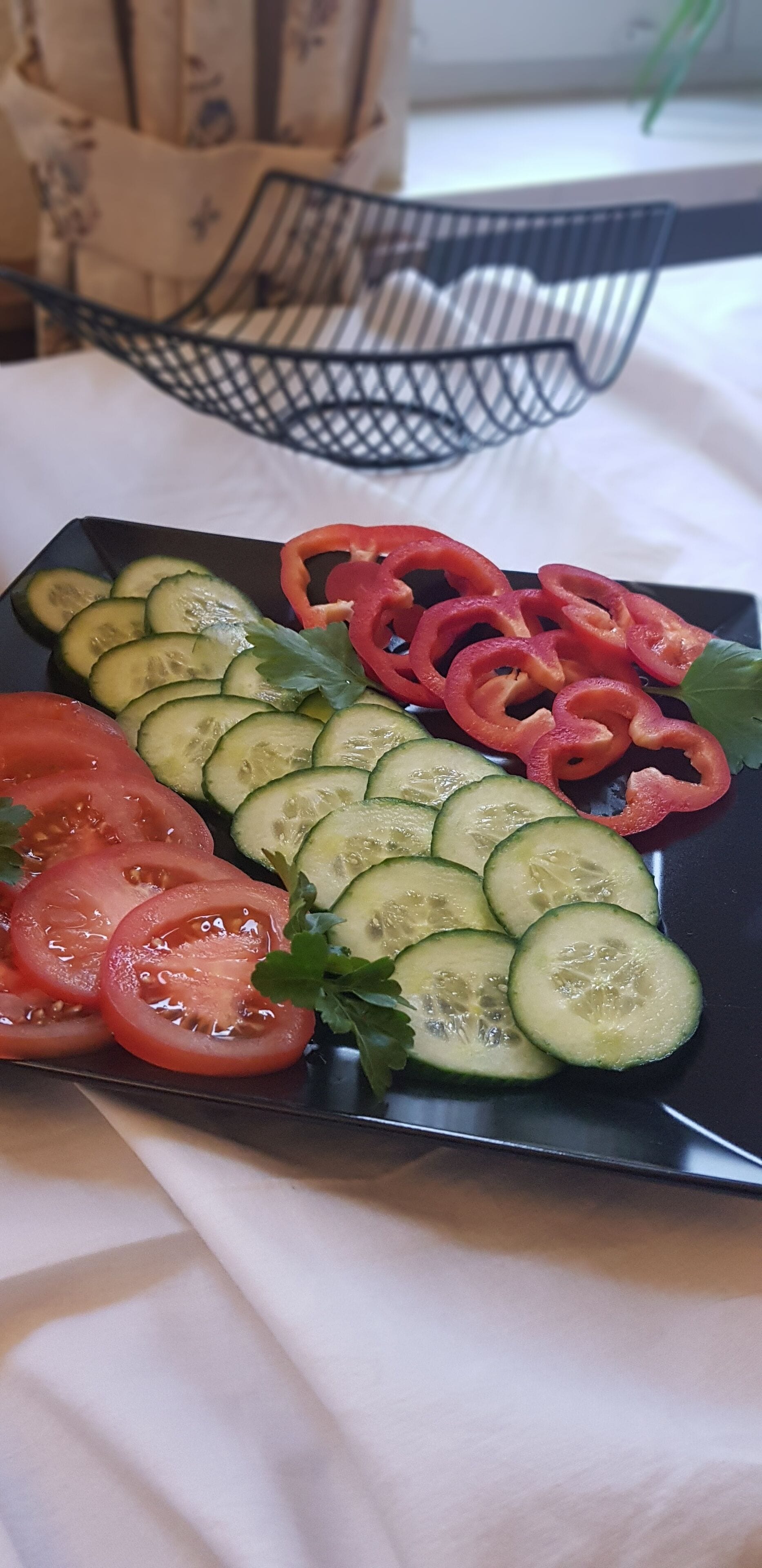 Ein Teller mit geschnittenen Gemüsestücken, darunter Gurken, Tomaten und rote Paprika, auf einer schwarzen Platte.