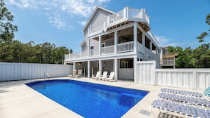 Une maison à deux étages avec une piscine, des chaises longues et une clôture blanche.