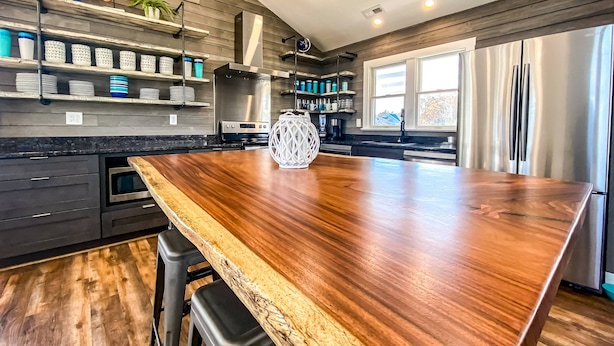 Une cuisine moderne dotée d’un grand îlot central en bois, d’appareils électroménagers intégrés et offrant une vue sur l’extérieur.