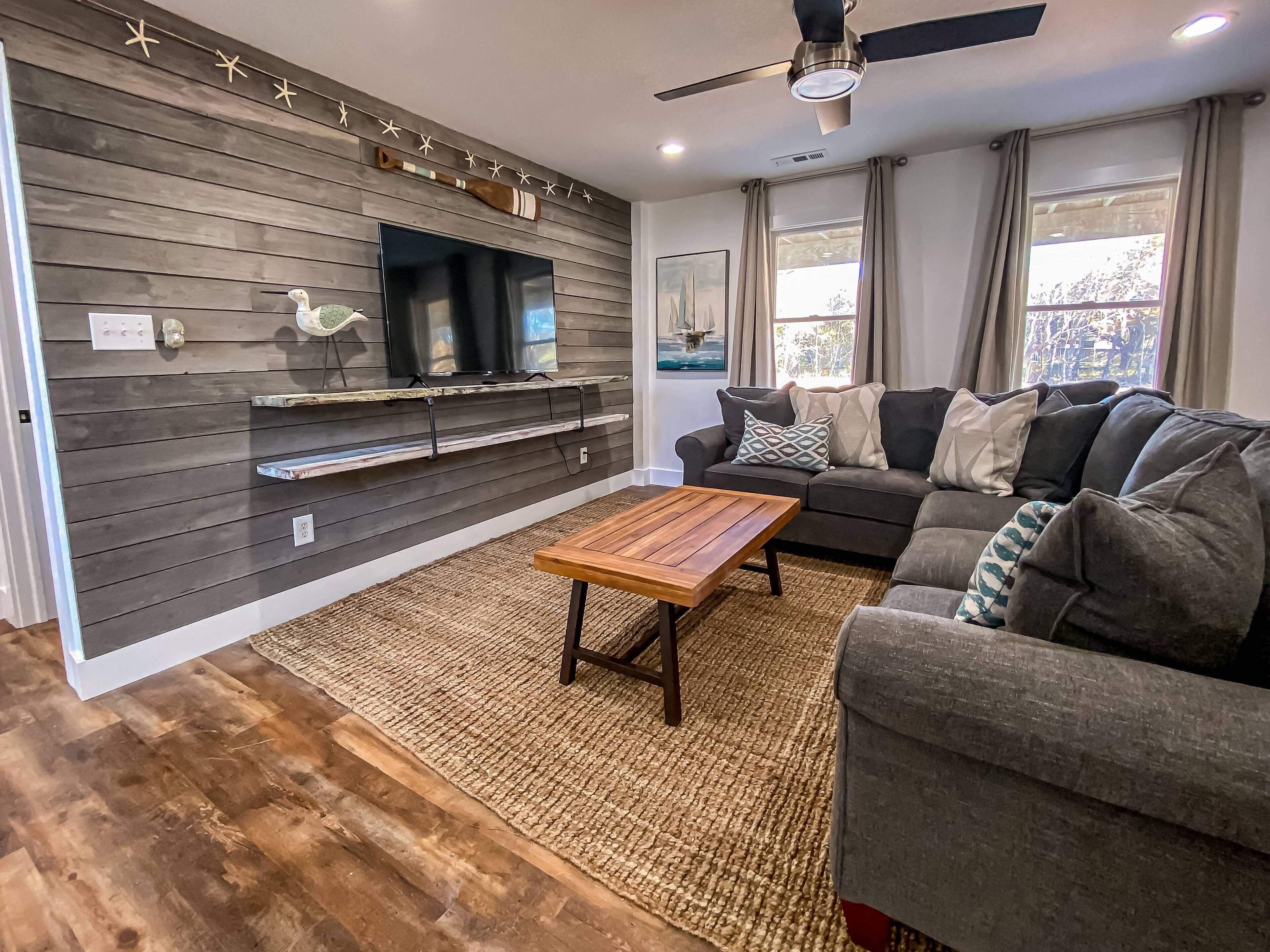 Ein modernes Wohnzimmer mit grauem Sofa, einem Holztisch und einem an einer Holzwand befestigten Fernseher.