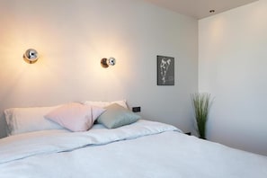 A bedroom with a bed, two wall-mounted light fixtures, a framed artwork, and a potted plant. - Vesturgata (Reykjavik)