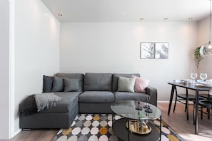 A modern living room with a grey sectional sofa, a glass coffee table, and a dining area with a black table and chairs. - Vesturgata (Reykjavik)