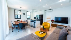 Uma sala de estar moderna com um sofá, uma poltrona amarela, uma mesa de jantar com cadeiras e uma área de cozinha com televisão.