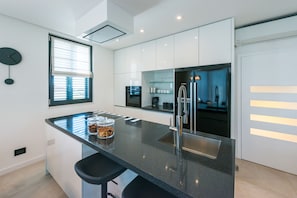 A modern kitchen with a black countertop, stainless steel appliances, and a window with blinds.