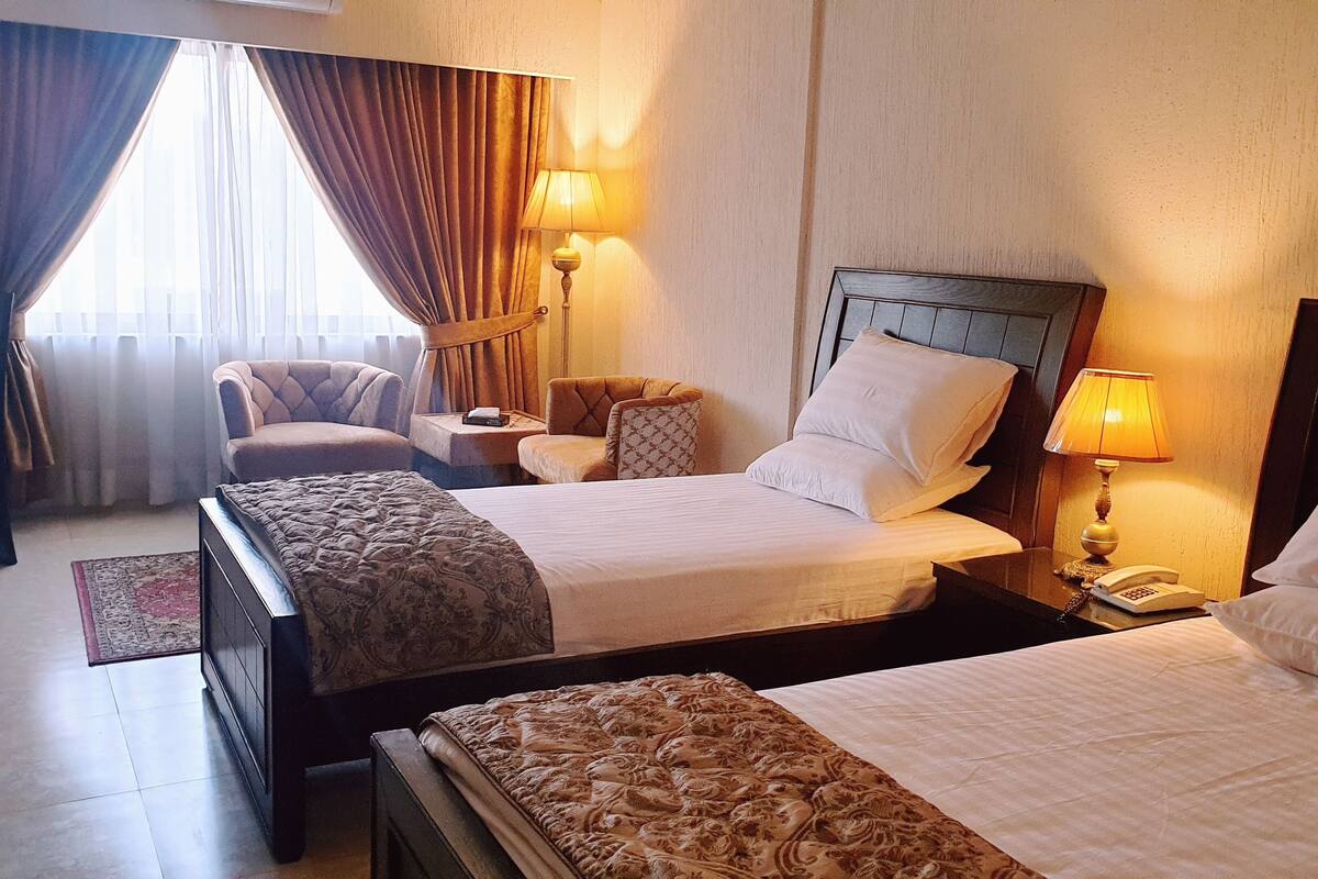 Une chambre d’hôtel avec deux lits, une chaise, une table de chevet et une lampe.