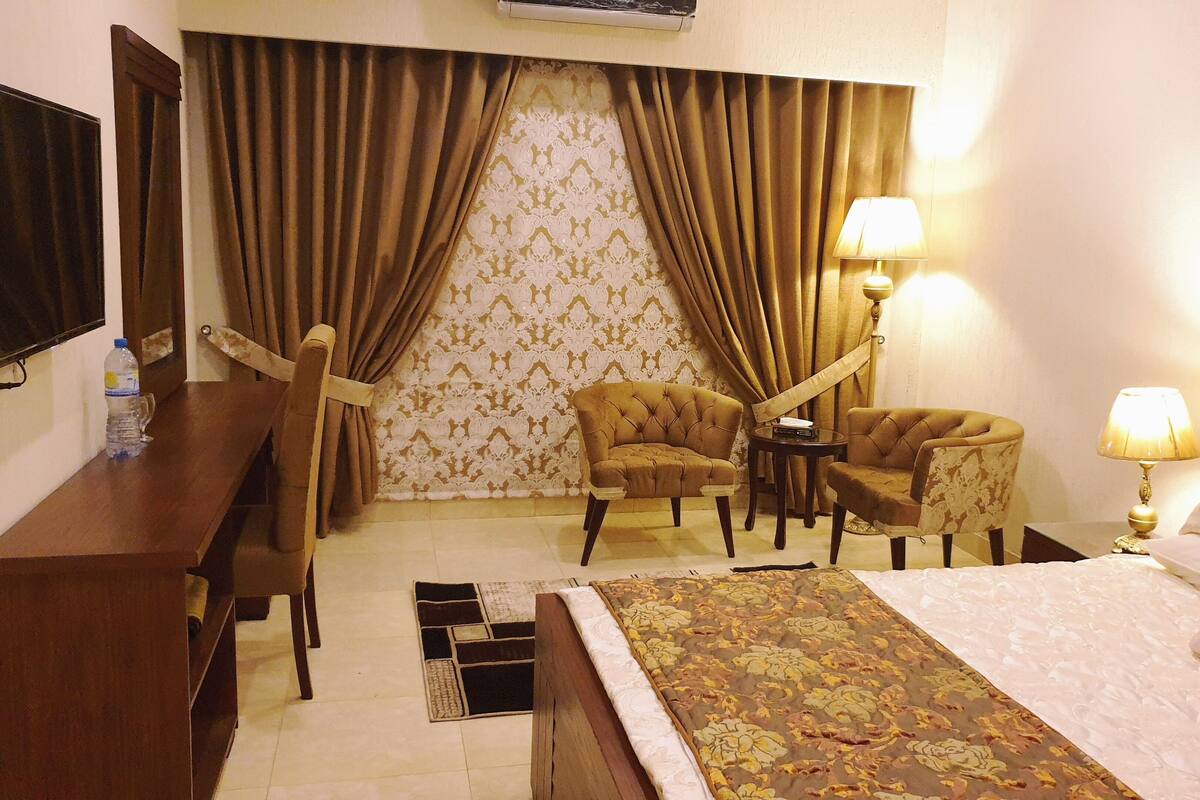 Une chambre d’hôtel comprenant un lit, deux fauteuils, une petite table, un bureau, une lampe et un téléviseur.