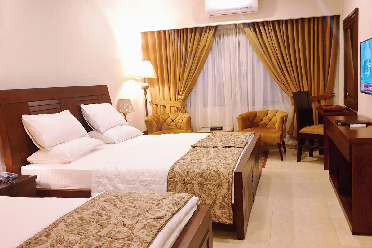 Une chambre d’hôtel avec un grand lit, deux tables de chevet, un bureau avec une chaise, une télévision et une fenêtre avec des rideaux.