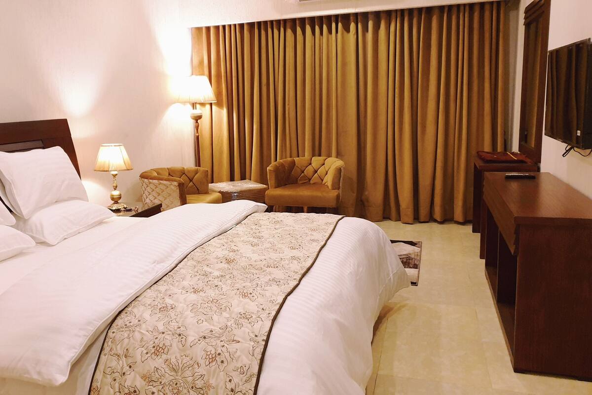 Une chambre d’hôtel avec un grand lit, un bureau, une chaise, une lampe et un téléviseur.