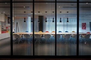 A conference room with a long table and multiple chairs, large windows with blinds, and a visible ladder.